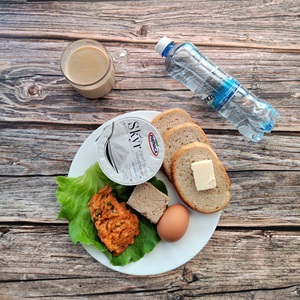 Zdjęcie przedstawia dietę podstawową Jogurt typu islandzkiego naturalny Skyr Chleb mieszany pszenno-żytni Masło extra Pasztet wołowo-drobiowy Jajko gotowane Pasta warzywna Sałata zielona Kawa zbożowa z mlekiem Woda mineralna